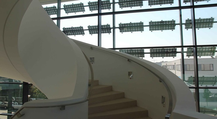 Eine Wendeltreppe mit geschlossener Brüstung vermittelt den Eindruck von Galerie oder Theater. Überall in dem Atrium ist die Photovoltaikanlage vor der Gasfassade allgegenwärtig. - © William Vorsatz
