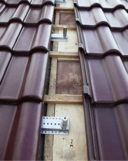 
Lässt sich der Halter wegen der Ziegelöffnung nicht in der Nähe des Aufnahmedorns befestigen, wird ein Stützbrett zwischen den Latten untergebaut und fixiert.
