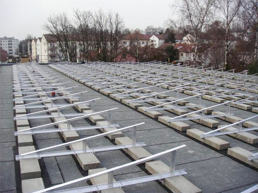 



Vor der Auflage der Solarmodule sind die Gestelle vorschriftsmäßig montiert und mit Betonplatten ballastiert.Die Steine liegen auf speziellen Schutzmatten, um das Dach zu schonen.
