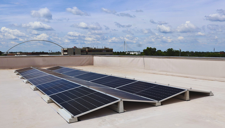 Auf einem Flachdach installierte Solarmodule mit einer Stadtlandschaft und einem bewölkten Himmel im Hintergrund. - © Basic