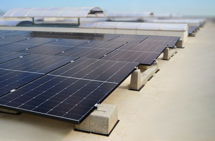 Reihen von Solarmodulen auf einem Flachdach unter freiem Himmel. - © Basic