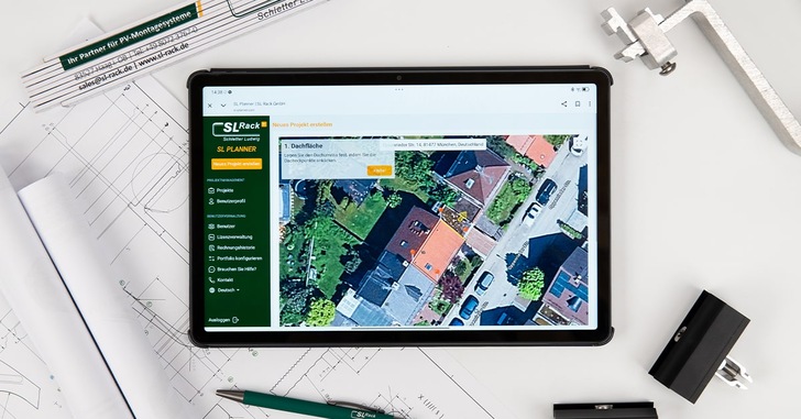 Ein Tablet zeigt eine Satellitenkartenansicht von Häusern an und stützt sich dabei auf architektonische Entwürfe und Zeichenwerkzeuge. - © SL Rack