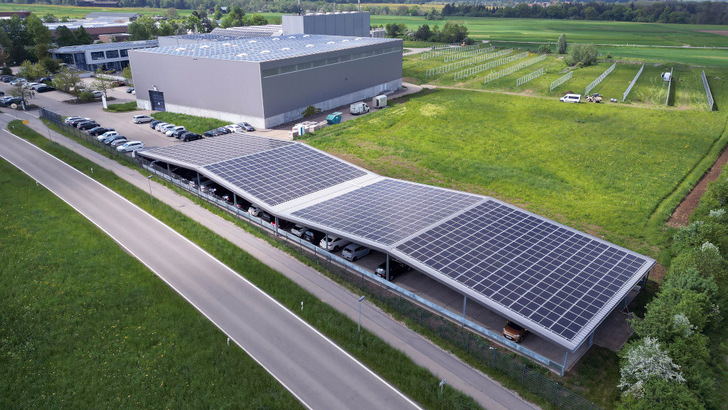 Das riesige Solardach über dem Parkplatz liefert nicht nur Strom, sondern schützt auch die Autos. Rechts im Hintergrund steht die vertikal aufgeständerte Freiflächenanlage. - © Hörmann
