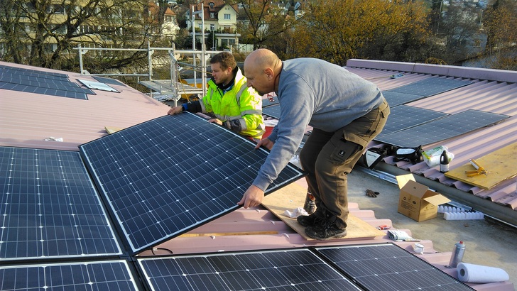 Installateure verkleben die leichten Module auf einem Trapezblechdach. - © LEC Leutenegger Energie Control
