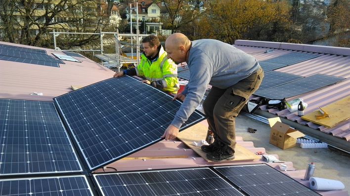 Installateure verkleben die leichten Module auf einem Trapezblechdach.